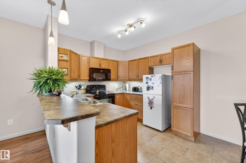Kitchen featuring wood-finish cabinetry, a large kitchen island with integrated sink, stone-finish countertops, tile flooring, and wood-finish flooring - 133 2503 Hanna Crescent, Edmonton, AB 
