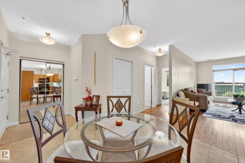 Open-concept dining area featuring a glass-top table, tile flooring, and a contemporary chandelier - 133 2503 Hanna Crescent, Edmonton, AB 