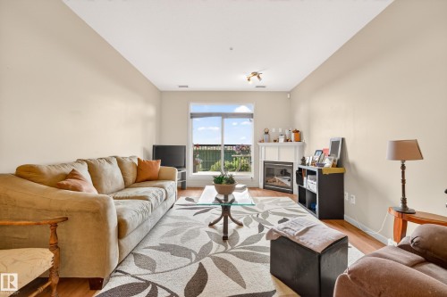Living area featuring wood-finish flooring, a fireplace with a white mantel, and a large window with outdoor visibility - 133 2503 Hanna Crescent, Edmonton, AB 