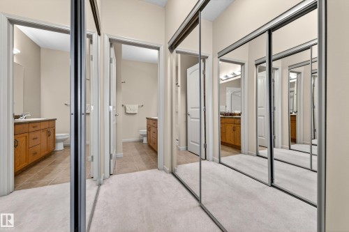 Hallway featuring mirrored closet doors, neutral carpet flooring, and two separate bathrooms - 133 2503 Hanna Crescent, Edmonton, AB 