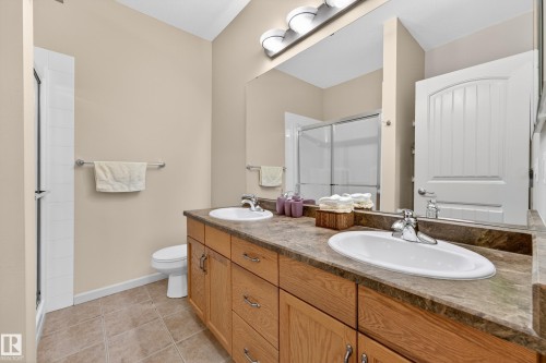Bathroom featuring a dual vanity with light wood cabinetry, stone-finish countertop, and undermount sinks - 133 2503 Hanna Crescent, Edmonton, AB 