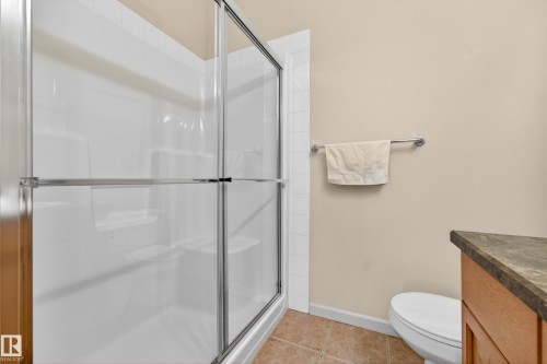 Shower enclosure with sliding glass doors, integrated shelving, tiled flooring, and a towel bar - 133 2503 Hanna Crescent, Edmonton, AB 