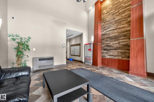 Spacious entry lobby featuring a stone accent wall, decorative wood columns, patterned tile flooring, and integrated wall lighting - 133 2503 Hanna Crescent, Edmonton, AB 