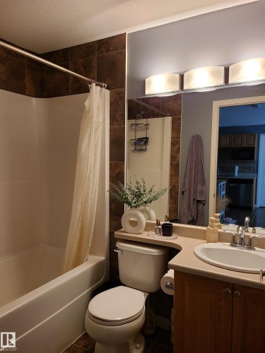 Full bathroom featuring a white tub/shower combination with dark ceramic tile surround, a built-in vanity with a light-colored countertop, and a large wall-mounted mirror - 116 5005 165 Avenue, Edmonton, AB 