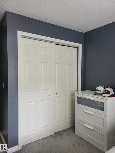 White bifold closet doors with paneled details, framed by white trim and a deep blue wall - 116 5005 165 Avenue, Edmonton, AB 