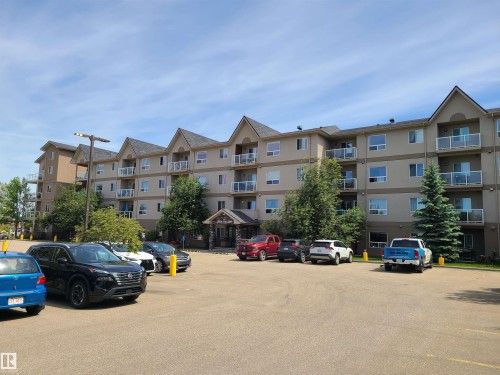Multi-story residential building featuring balconies with glass railings, an inviting entrance with stone accents, and ample paved surface parking - 116 5005 165 Avenue, Edmonton, AB 