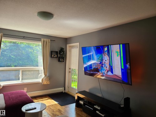 Living area featuring wood-finish flooring, a contemporary ceiling light fixture, and a large window with direct outdoor access - 116 5005 165 Avenue, Edmonton, AB 