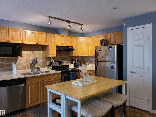 Kitchen featuring light wood cabinetry, stainless steel appliances, and a tiled backsplash - 116 5005 165 Avenue, Edmonton, AB 