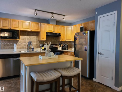 Kitchen featuring wood-finish cabinetry, stainless steel appliances, a tile backsplash, and a central island with countertop seating - 116 5005 165 Avenue, Edmonton, AB 