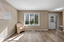 Spacious room featuring wood-finish flooring, neutral-toned walls, a large window with white blinds, a white entry door with a sidelight, and a built-in bench - 