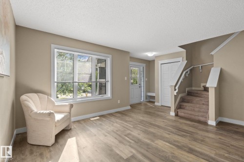 Spacious living area featuring wood-finish flooring, a large window, a neutral color palette, and a staircase with carpeted treads - 12809 203A, Edmonton, AB 