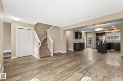 Expansive open-concept living area featuring wood-finish flooring, neutral wall tones, and a staircase with carpeted treads and white railings - 