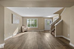 Spacious living area featuring wood-finish flooring, neutral wall tones, and white trim - 