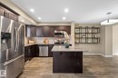 Open-concept kitchen featuring dark wood cabinetry, stainless steel appliances, light-toned countertops, and wood-finish flooring - 12809 203A, Edmonton, AB 