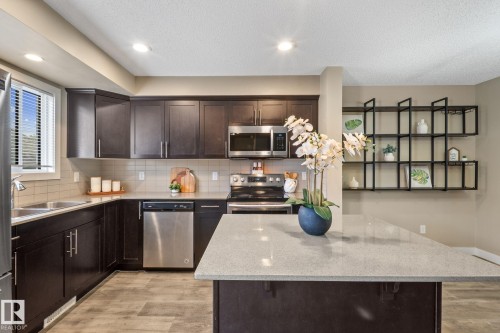 Contemporary kitchen featuring dark wood cabinetry, stainless steel appliances, light-toned countertops, and wood-finish flooring - 12809 203A, Edmonton, AB 