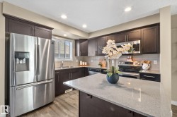 Functional kitchen featuring dark wood-finish cabinetry, stainless steel appliances, a light-toned countertop, and wood-finish flooring - 