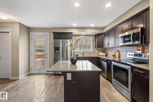 Modern kitchen featuring dark wood cabinetry, stainless steel appliances, a center island with a light-toned countertop, and wood-finish flooring - 12809 203A, Edmonton, AB 