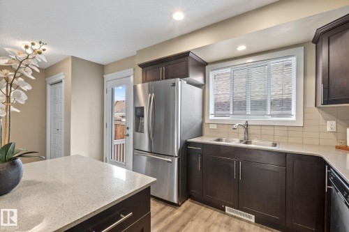 Kitchen featuring dark wood cabinetry, light-toned countertops, stainless steel appliances, and wood-finish flooring - 12809 203A, Edmonton, AB 