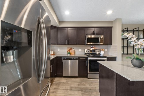 Modern kitchen featuring dark wood cabinetry, stainless steel appliances, a light-toned countertop, subway tile backsplash, and wood-finish flooring - 12809 203A, Edmonton, AB 