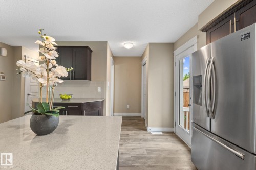Kitchen featuring a spacious light-toned countertop, dark wood-finish cabinetry, a built-in stainless steel refrigerator, wood-finish flooring, and a glass-paned door providing outdoor access - 12809 203A, Edmonton, AB 