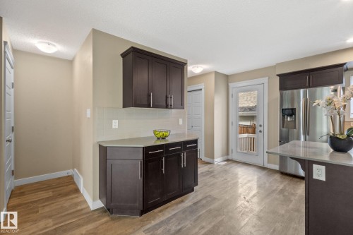 Kitchen featuring wood-finish flooring, dark wood cabinetry, light countertops, and a full-light exterior door - 12809 203A, Edmonton, AB 
