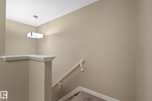 Stairwell featuring a rectangular pendant light, textured ceiling, a built-in display ledge with crown molding, a white handrail, and carpeted stairs - 12809 203A, Edmonton, AB 
