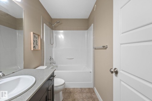Contemporary bathroom featuring a white panel door, a dark wood-finish vanity with a light countertop, an undermount sink, a white toilet, and a white shower/tub combination with chrome fixtures - 12809 203A, Edmonton, AB 