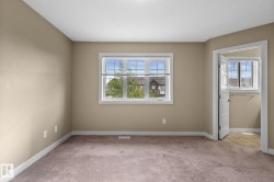 Neutral-toned room featuring a large window with white blinds, light brown carpeting, and white trim - 