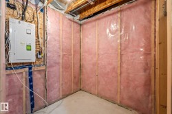 Unfinished basement area featuring framed walls with insulation and vapor barrier, exposed ceiling joists, and a concrete floor - 