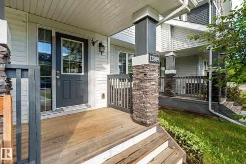 Covered front porch featuring wood-finish flooring, stone-clad pillars, and a dark paneled door with glass inserts - 12809 203A, Edmonton, AB 