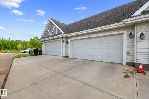 Two-car garage with white paneled doors, light grey siding, dark grey roof shingles, a decorative gable, and exterior wall sconces - 12809 203A, Edmonton, AB 