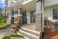 Covered front porch featuring wood-finish decking and steps, stone veneer column accents, and a panel-style entry door - 