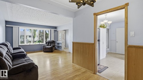 Living area featuring wood-finish flooring, a large bay window, and light blue wall paint - 13008 105 Street Nw, Edmonton, AB 