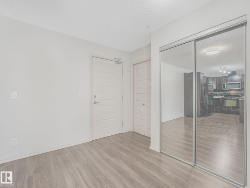 Wood-finish flooring throughout, featuring a five-panel entry door with brushed nickel hardware - 117 6070 Schonsee Way, Edmonton, AB 