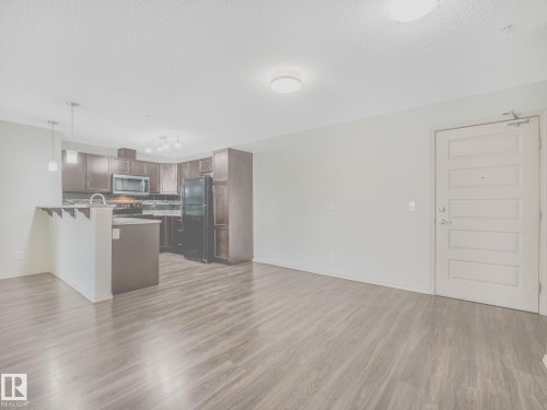 Open-concept living area featuring wood-finish flooring, a kitchen with dark cabinetry, black appliances, and pendant lighting - 117 6070 Schonsee Way, Edmonton, AB 