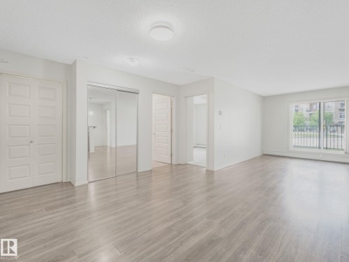 Spacious room featuring wood-finish flooring, white walls, and a sliding glass door providing external exposure - 117 6070 Schonsee Way, Edmonton, AB 