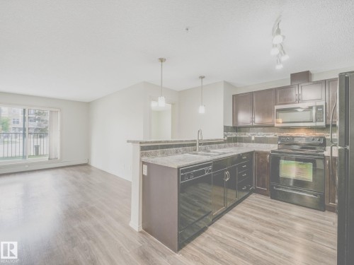 Kitchen featuring wood-finish flooring, dark cabinetry, and black appliances - 117 6070 Schonsee Way, Edmonton, AB 