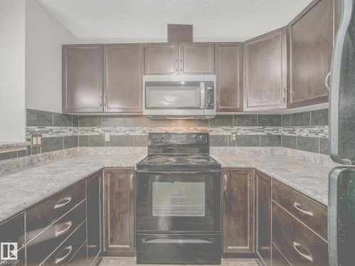 U-shaped kitchen featuring dark wood cabinetry, a stainless steel microwave, black electric range, and a decorative tile backsplash with mosaic accents - 117 6070 Schonsee Way, Edmonton, AB 