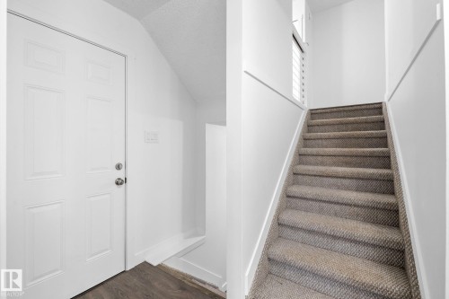 Entryway featuring a paneled door with polished hardware, wood-finish flooring, and a carpeted staircase with white risers and handrails - 2832 135 Avenue, Edmonton, AB - Indoor Photo Showing Other Room