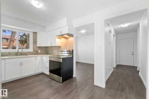 Modern kitchen featuring white cabinetry, light-toned countertops, a stainless steel electric range with an overhead hood, and wood-finish flooring - 2832 135 Avenue, Edmonton, AB - Indoor Photo Showing Kitchen