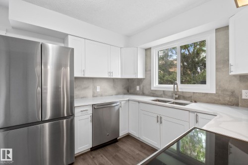 Modern kitchen featuring white cabinetry, stainless steel appliances, light-toned countertops, a stainless steel double sink with a gooseneck faucet, and wood-finish flooring - 2832 135 Avenue, Edmonton, AB - Indoor Photo Showing Kitchen With Double Sink