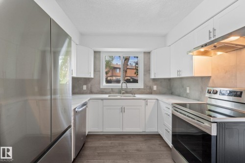 U-shaped kitchen featuring white shaker cabinetry, stainless steel appliances, stone-look countertops, a tile backsplash, and wood-finish flooring - 2832 135 Avenue, Edmonton, AB - Indoor Photo Showing Kitchen With Double Sink