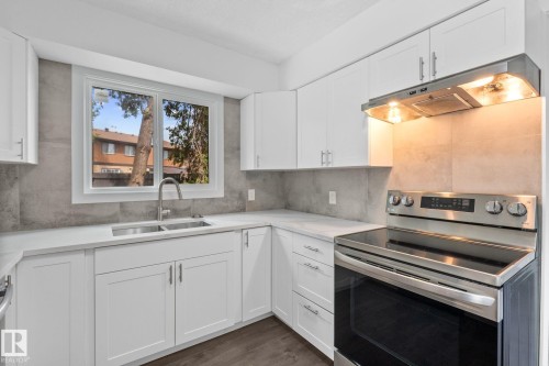 Modern kitchen featuring white shaker cabinetry, stainless steel appliances, a double basin sink with a gooseneck faucet, light-toned countertops, and a full-height tile backsplash - 2832 135 Avenue, Edmonton, AB - Indoor Photo Showing Kitchen With Double Sink
