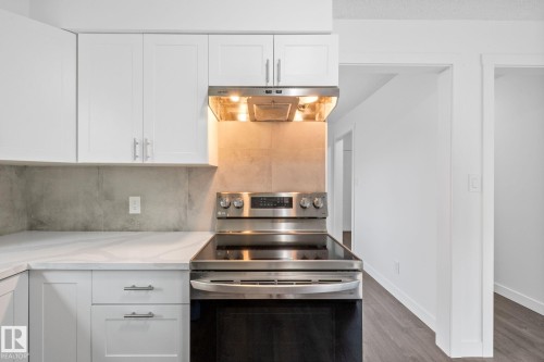 Modern kitchen featuring white shaker cabinetry, stainless steel electric range with overhead hood, light-toned backsplash, and white countertops - 2832 135 Avenue, Edmonton, AB - Indoor Photo Showing Kitchen