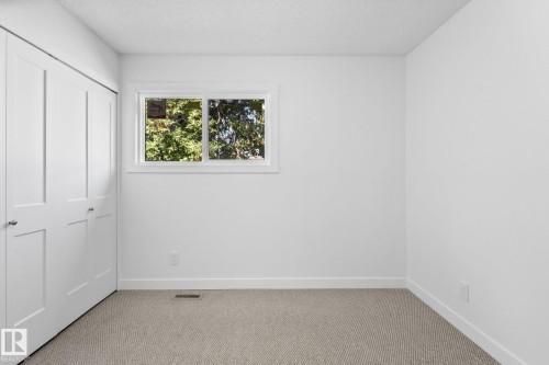 Neutral-toned carpeted room featuring a white paneled bi-fold closet, white window trim, and white baseboards - 2832 135 Avenue, Edmonton, AB - Indoor Photo Showing Other Room