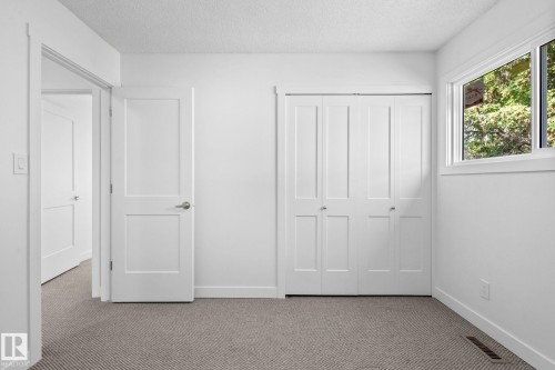White interior featuring textured carpet flooring, trim and baseboards, a window with exterior foliage, and a closet with bifold doors - 2832 135 Avenue, Edmonton, AB - Indoor Photo Showing Other Room
