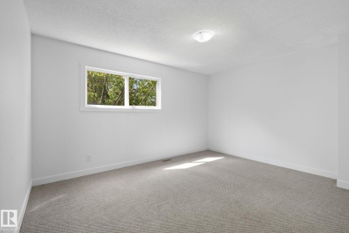 Neutral room featuring a window with exterior foliage, wall-to-wall carpeting, white baseboards, and a semi-flush mount ceiling light - 2832 135 Avenue, Edmonton, AB - Indoor Photo Showing Other Room