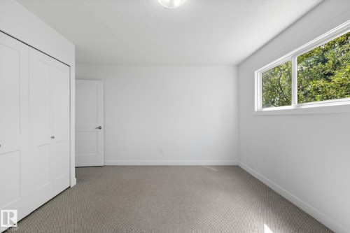 Bright interior space featuring a window with exterior tree views, neutral carpeting, white walls, and a flush-mount ceiling light - 2832 135 Avenue, Edmonton, AB - Indoor Photo Showing Other Room