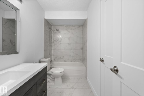Bathroom featuring a modern vanity with integrated sink, a deep soaking tub, patterned tile surround, and polished chrome fixtures - 2832 135 Avenue, Edmonton, AB - Indoor Photo Showing Bathroom