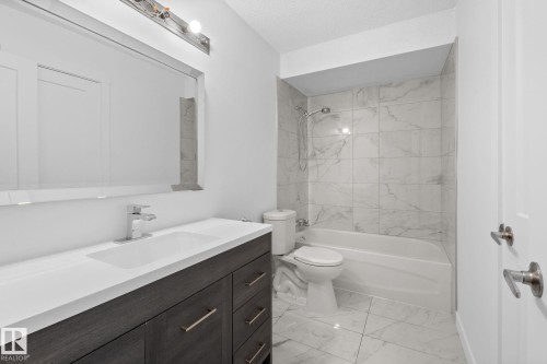 Contemporary bathroom featuring a dark wood-finish vanity with a white countertop and integrated sink, a large wall-mounted mirror, and a sleek chrome faucet - 2832 135 Avenue, Edmonton, AB - Indoor Photo Showing Bathroom
